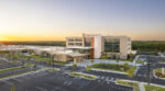 Exterior view of Prisma Health Northeast Medical Park in Columbia, South Carolina, showing a modern multi-story medical building with a glass entrance, covered drop-off area, landscaped grounds, and a large parking lot at sunrise.